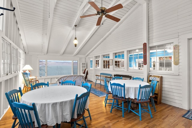 dining area with high vaulted ceiling, wooden walls, beamed ceiling, ceiling fan, and light hardwood / wood-style floors