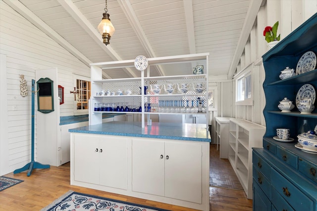 kitchen featuring light hardwood / wood-style flooring, wooden walls, lofted ceiling with beams, white cabinets, and decorative light fixtures