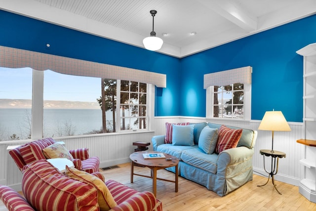 living room featuring wood-type flooring, a water view, a healthy amount of sunlight, and beam ceiling