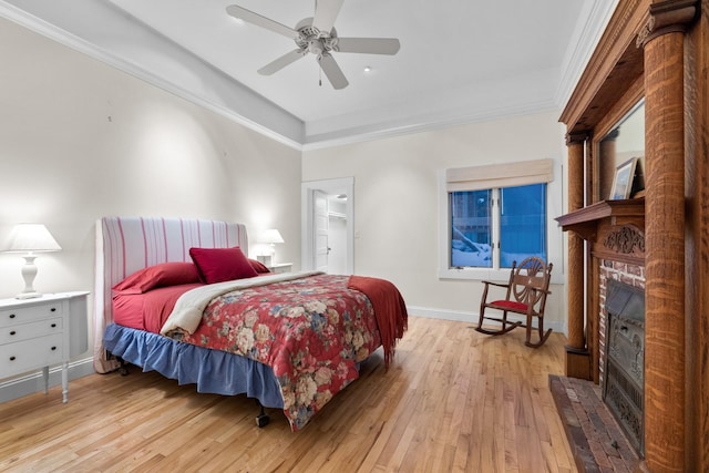 bedroom featuring crown molding, a walk in closet, a brick fireplace, light hardwood / wood-style flooring, and ceiling fan