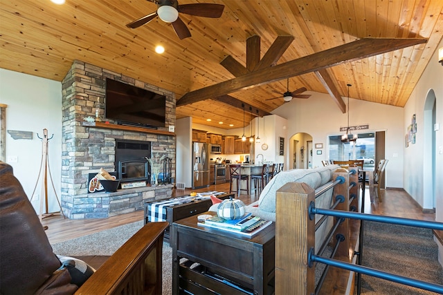 living room with wood ceiling, hardwood / wood-style floors, ceiling fan, beamed ceiling, and a stone fireplace