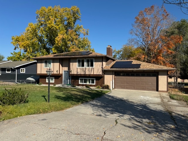 bi-level home featuring a front yard, solar panels, and a garage