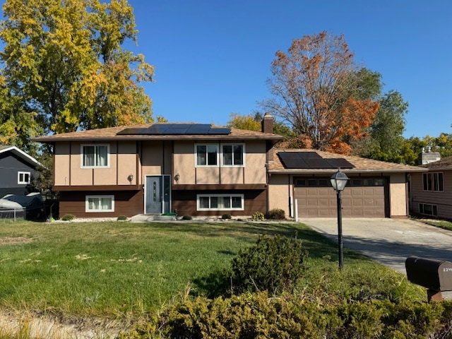 split foyer home featuring solar panels, a front lawn, and a garage