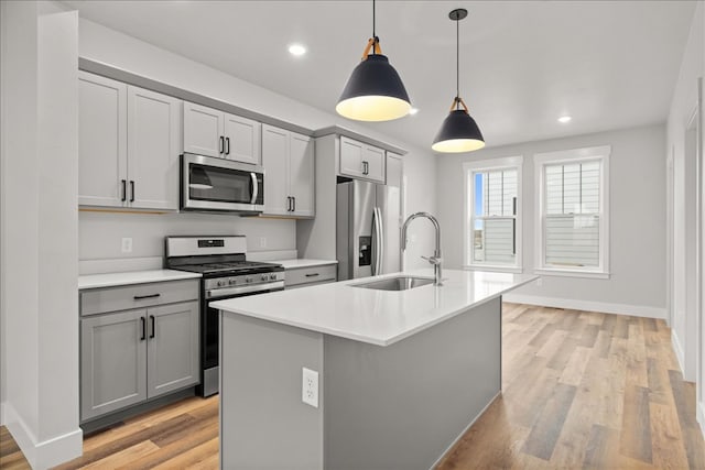 kitchen featuring decorative light fixtures, gray cabinetry, appliances with stainless steel finishes, and a center island with sink