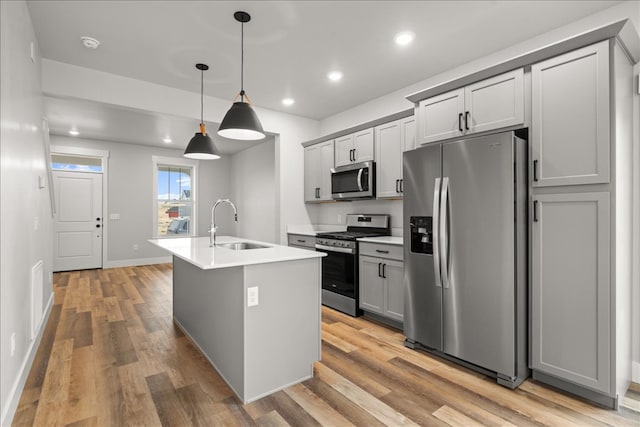 kitchen with gray cabinetry, stainless steel appliances, pendant lighting, a center island with sink, and light wood-type flooring