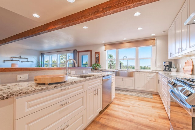 kitchen with appliances with stainless steel finishes, beamed ceiling, white cabinetry, sink, and light stone counters