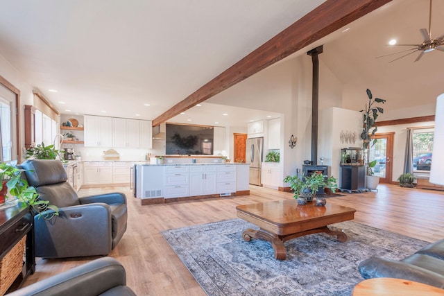 living room with light hardwood / wood-style flooring, ceiling fan, beam ceiling, high vaulted ceiling, and a wood stove