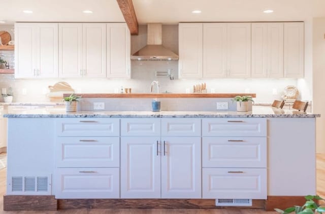 kitchen with beamed ceiling, white cabinetry, sink, light stone counters, and wall chimney exhaust hood