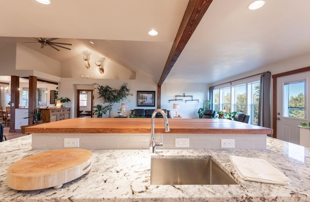 kitchen with lofted ceiling with beams, ceiling fan, light stone countertops, and sink