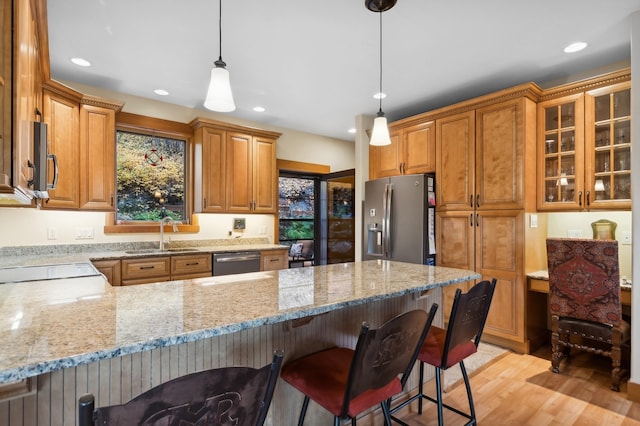 kitchen featuring light stone counters, stainless steel appliances, decorative light fixtures, sink, and light hardwood / wood-style floors