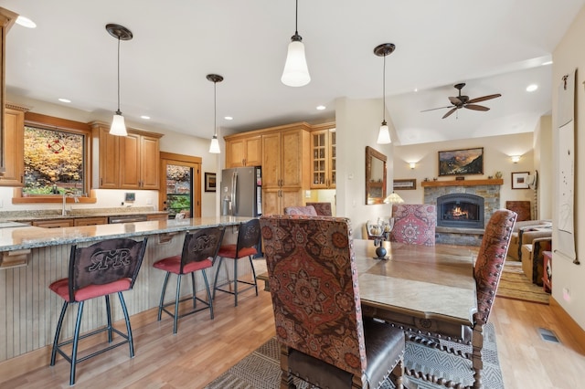 dining area featuring a fireplace, ceiling fan, and light hardwood / wood-style flooring