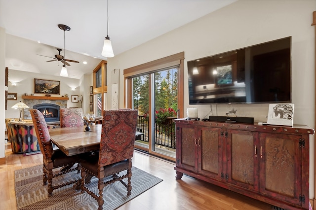 dining area with ceiling fan, a stone fireplace, light hardwood / wood-style flooring, and lofted ceiling