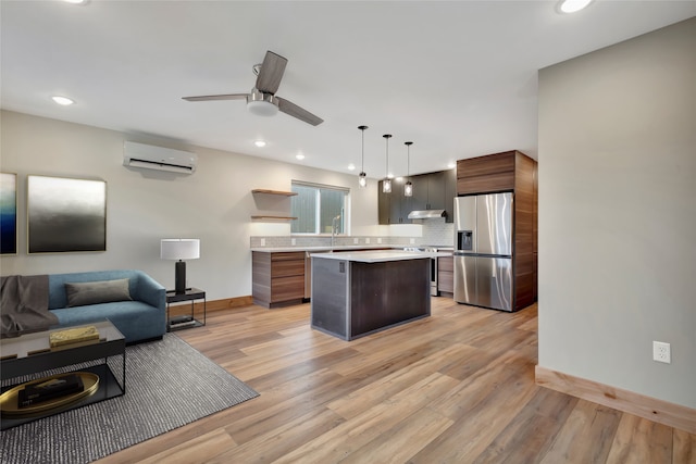 kitchen with light wood-type flooring, stainless steel appliances, a wall unit AC, decorative light fixtures, and a kitchen island