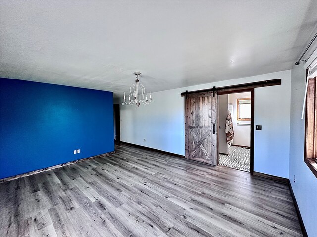 unfurnished room with a barn door, a notable chandelier, and wood-type flooring