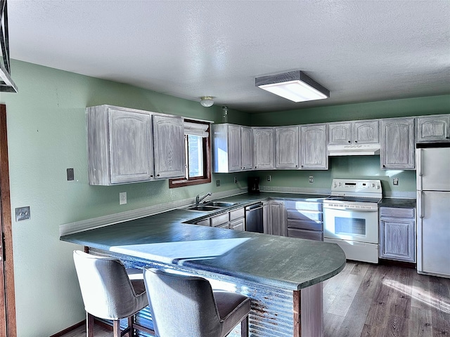 kitchen featuring kitchen peninsula, hardwood / wood-style floors, sink, and white appliances