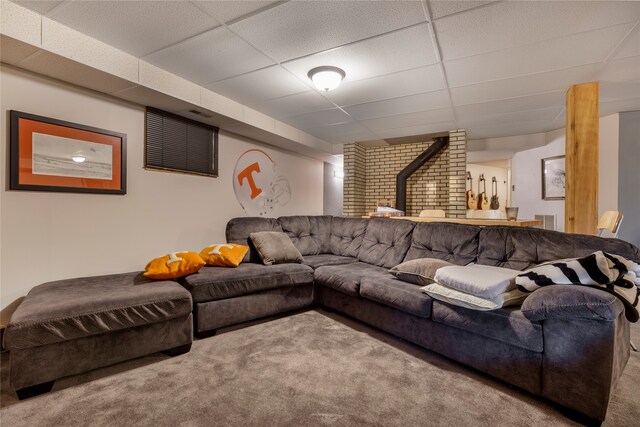 living room with a drop ceiling, carpet flooring, and a wood stove