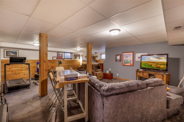 carpeted living room featuring a drop ceiling and wooden walls