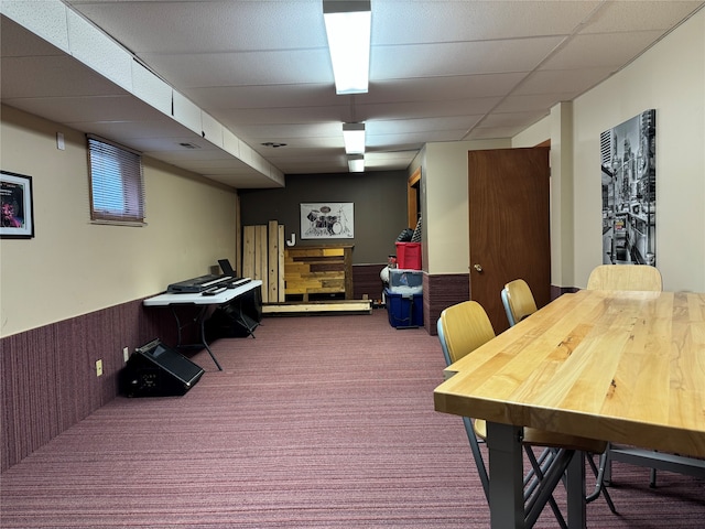 interior space with a paneled ceiling, carpet flooring, and wood walls