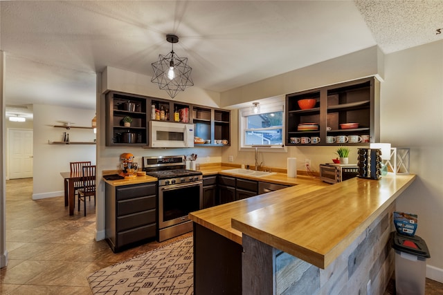 kitchen featuring butcher block counters, sink, gas stove, decorative light fixtures, and kitchen peninsula