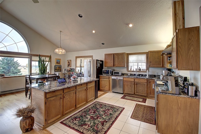 kitchen with stone countertops, high vaulted ceiling, sink, appliances with stainless steel finishes, and decorative light fixtures