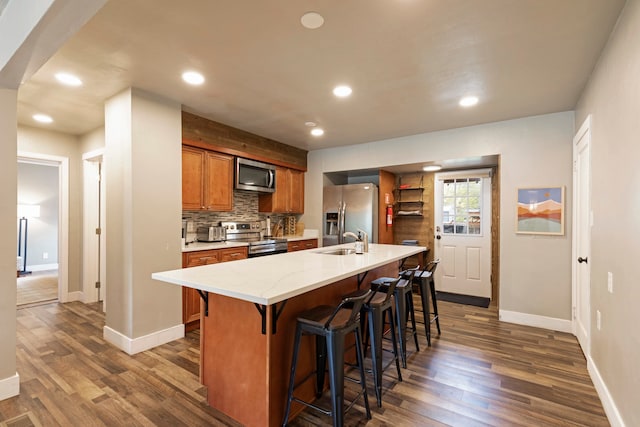 kitchen with appliances with stainless steel finishes, sink, an island with sink, a breakfast bar area, and dark hardwood / wood-style floors