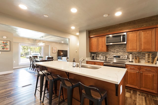 kitchen with dark hardwood / wood-style flooring, an island with sink, a kitchen bar, sink, and stainless steel appliances