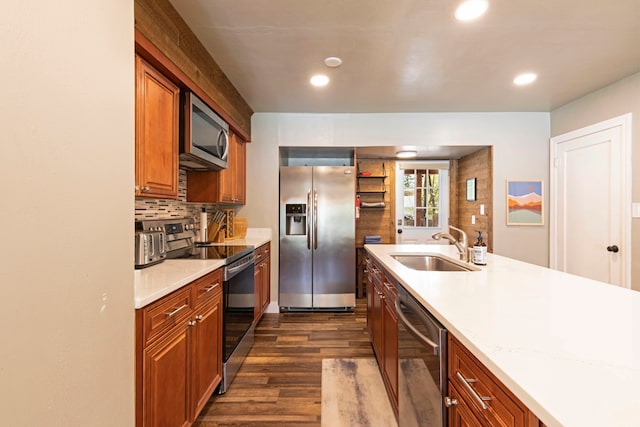 kitchen with appliances with stainless steel finishes, sink, light stone countertops, backsplash, and dark wood-type flooring