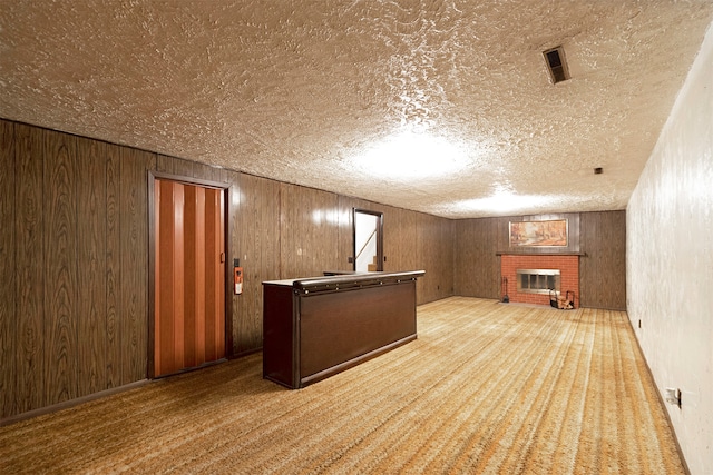 additional living space with wooden walls, a brick fireplace, a textured ceiling, and light colored carpet