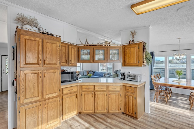 kitchen with a textured ceiling, kitchen peninsula, vaulted ceiling, light hardwood / wood-style flooring, and an inviting chandelier