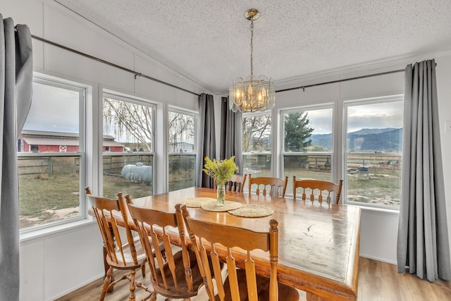 dining area with a textured ceiling, light hardwood / wood-style floors, vaulted ceiling, a mountain view, and a notable chandelier