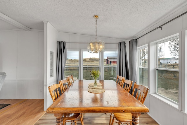 dining room with lofted ceiling, a notable chandelier, a textured ceiling, and light hardwood / wood-style floors