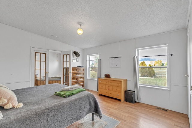 bedroom with a textured ceiling, multiple windows, and light wood-type flooring