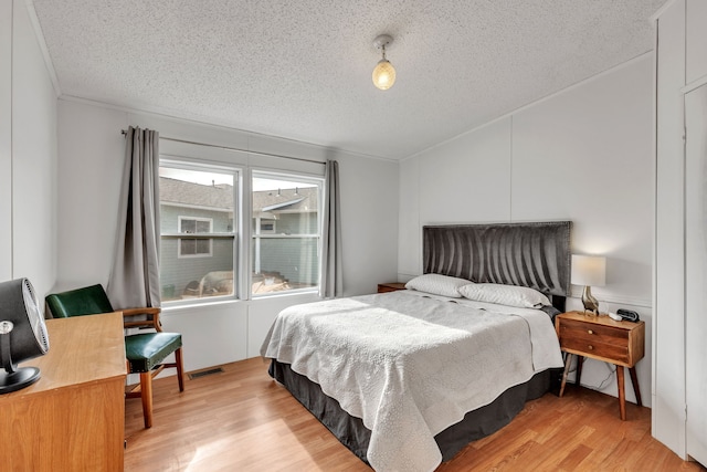 bedroom with ornamental molding, a textured ceiling, and light wood-type flooring