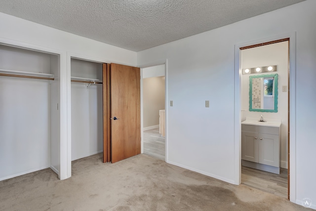 unfurnished bedroom featuring sink, ensuite bath, a textured ceiling, multiple closets, and light colored carpet