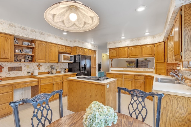 kitchen with sink, kitchen peninsula, stainless steel gas stovetop, a kitchen island, and black fridge with ice dispenser