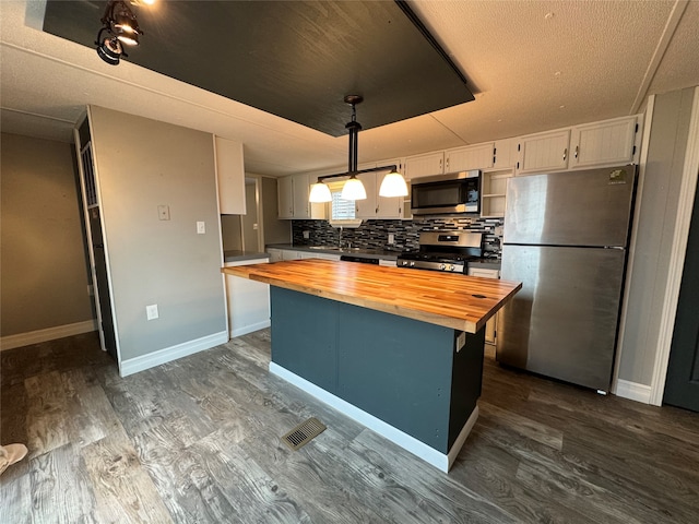 kitchen with butcher block countertops, white cabinetry, appliances with stainless steel finishes, decorative light fixtures, and dark hardwood / wood-style flooring