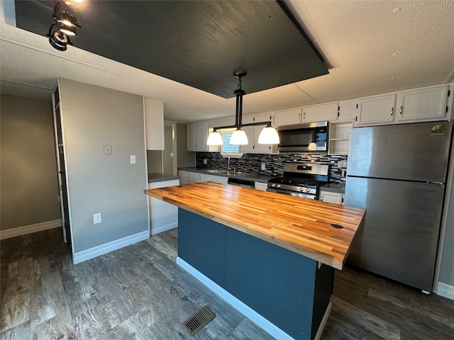 kitchen with butcher block countertops, white cabinetry, appliances with stainless steel finishes, pendant lighting, and decorative backsplash