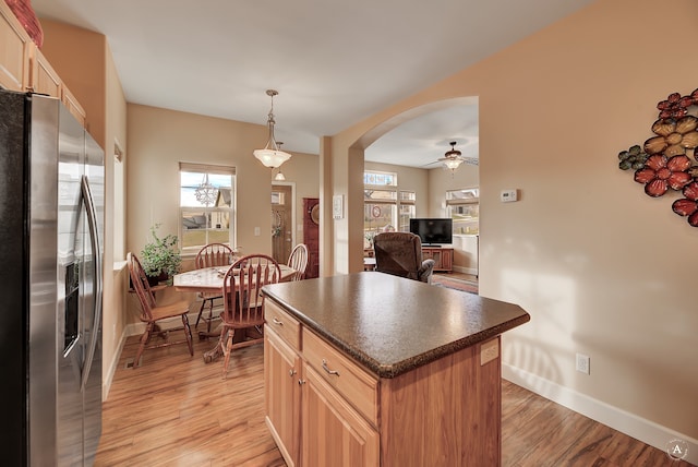 kitchen with ceiling fan, hanging light fixtures, a kitchen island, stainless steel fridge, and light wood-type flooring