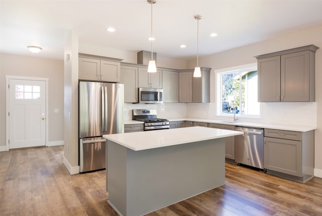 kitchen featuring light hardwood / wood-style floors, stainless steel appliances, a center island, gray cabinets, and hanging light fixtures