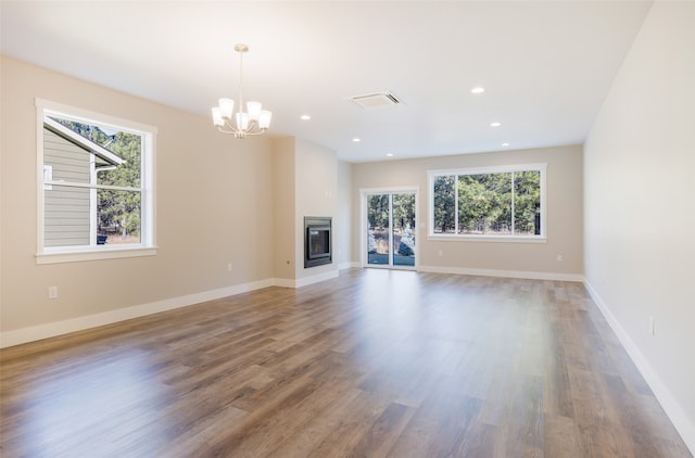 unfurnished living room featuring a notable chandelier, a healthy amount of sunlight, and wood-type flooring