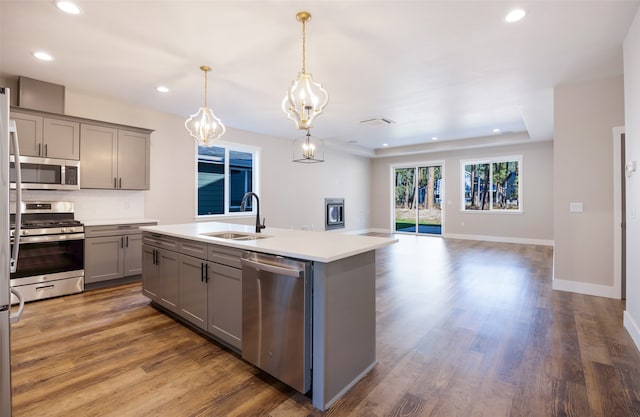 kitchen featuring sink, stainless steel appliances, pendant lighting, gray cabinets, and a kitchen island with sink