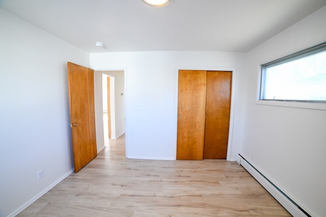 unfurnished bedroom featuring light hardwood / wood-style floors, a closet, and a baseboard heating unit