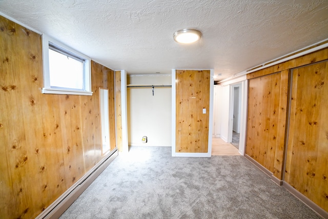 basement featuring wood walls, baseboard heating, a textured ceiling, and carpet