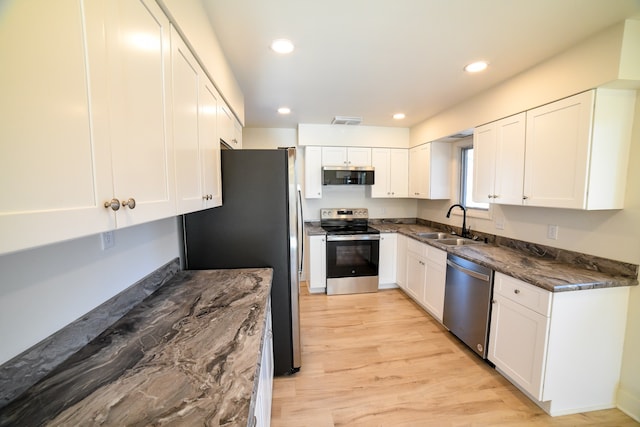 kitchen featuring stainless steel appliances, sink, white cabinets, dark stone countertops, and light hardwood / wood-style flooring