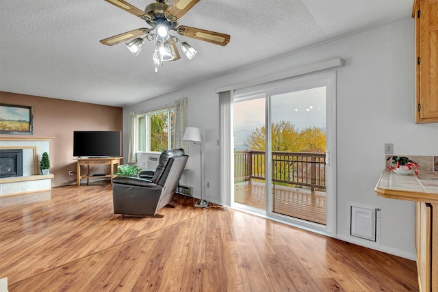 living room with light wood-type flooring, a tile fireplace, a textured ceiling, a ceiling fan, and a baseboard radiator