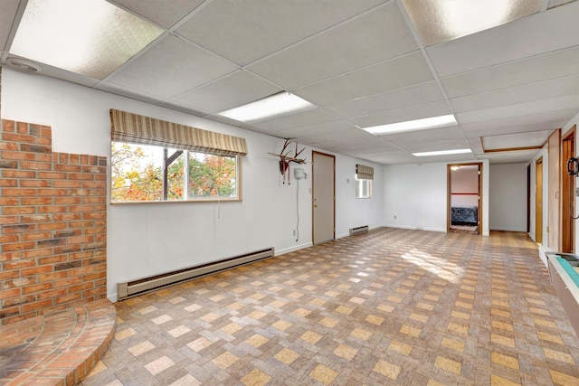 basement with baseboard heating, a paneled ceiling, and baseboards