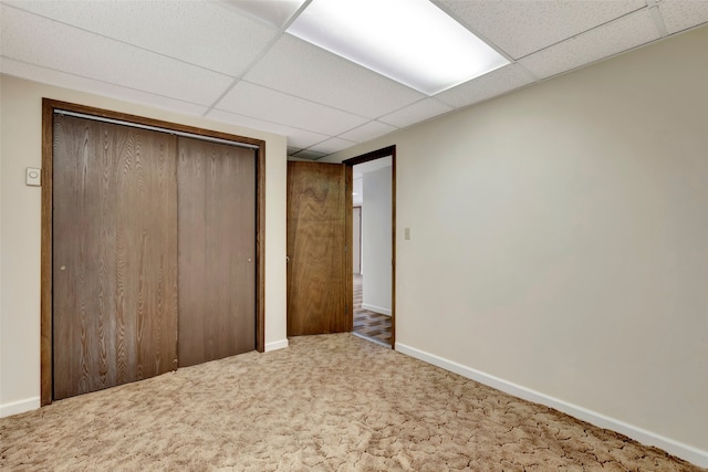 unfurnished bedroom featuring carpet floors, baseboards, a drop ceiling, and a closet