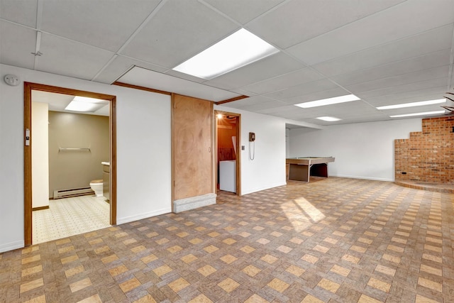 finished basement with a baseboard heating unit, a paneled ceiling, and baseboards