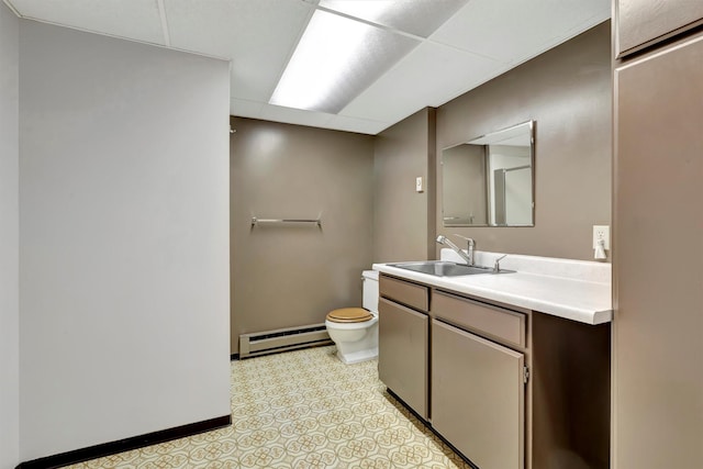 bathroom featuring toilet, a drop ceiling, a baseboard heating unit, baseboards, and vanity