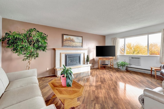 living area with a tiled fireplace, a textured ceiling, wood finished floors, a baseboard heating unit, and a wall unit AC